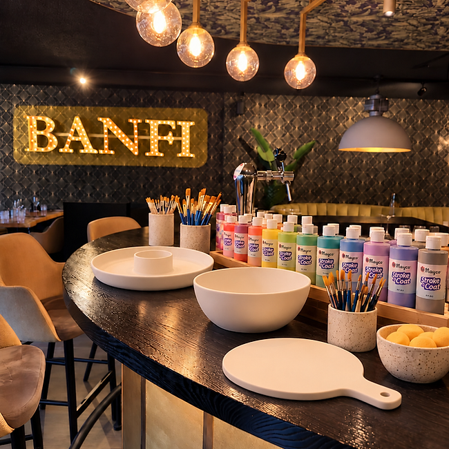 Keramiek-workshop op de bar van Banfi: ongeverfde schalen, bakjes glazuur en penselen onder het verlichte BANFI-bord